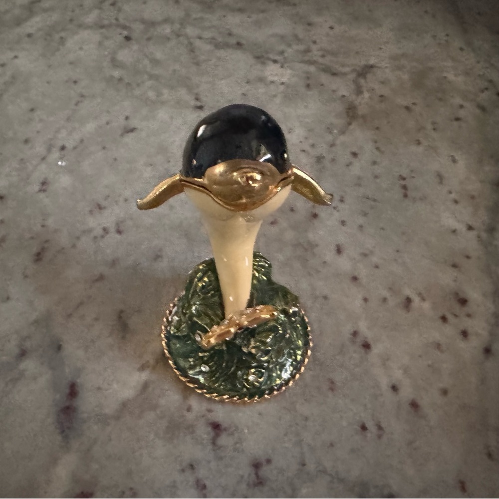 a blue dolphin, gold trim, a cream underbody sitting on a green stand trinket